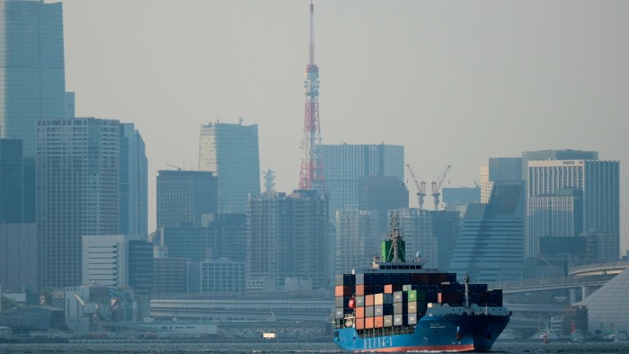 Tokyo Tower is seen amid tall buildings as a container ship leaves a cargo terminal in Tokyo