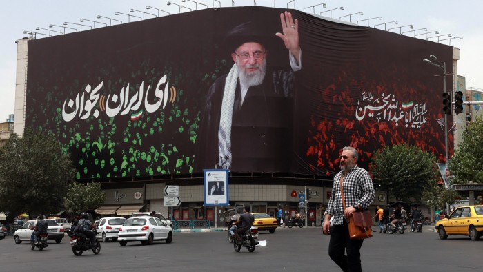 An Iranian crosses a street next to a billboard bearing the portrait of Iranian supreme leader Ayatollah Ali Khamenei