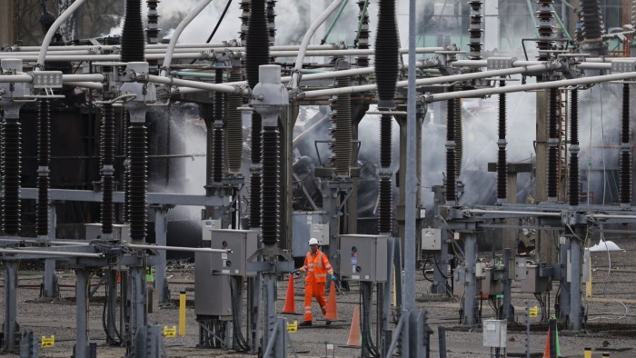 Workers walk on site as smoke rises from the North Hyde electrical substation which caught fire on March 21 and caused Heathrow airport to shut down