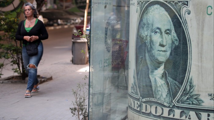 A woman walks past a storefront displaying a large-scale image of a US dollar banknote