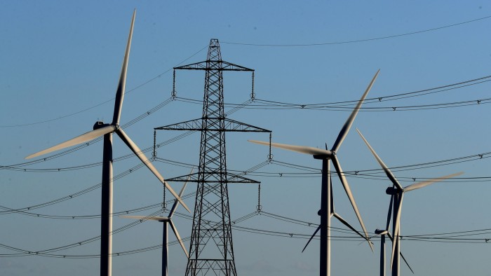 Wind turbines at a wind farm are visible among electricity pylons
