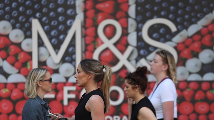 Shoppers pass a Marks and Spencer retail store in London