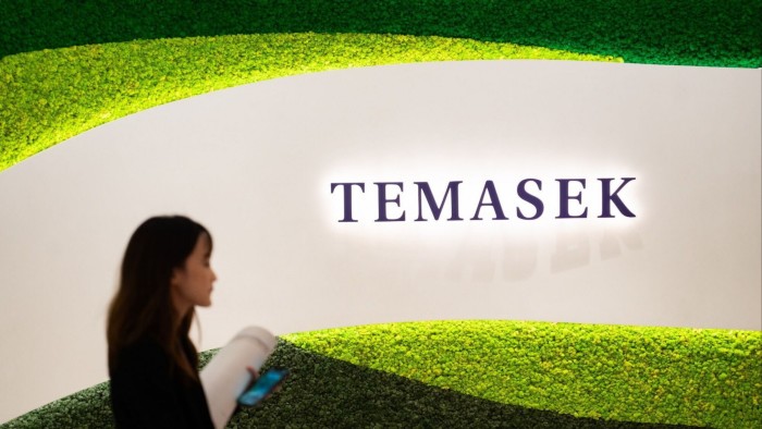 A woman walks past a brightly lit Temasek Holdings sign