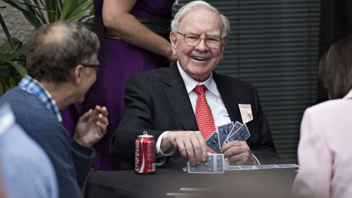 Warren Buffet smiles as he holds a hand of cards
