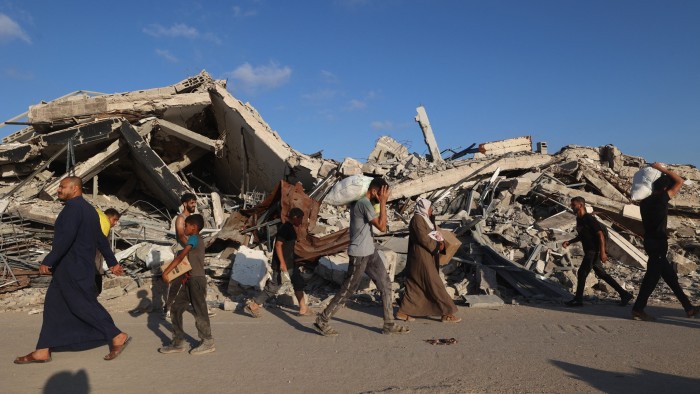 Palestinians, some carrying aid parcels, walking past destroyed buildings near the Nuseirat refugee camp in the central Gaza strip on June 25 2025